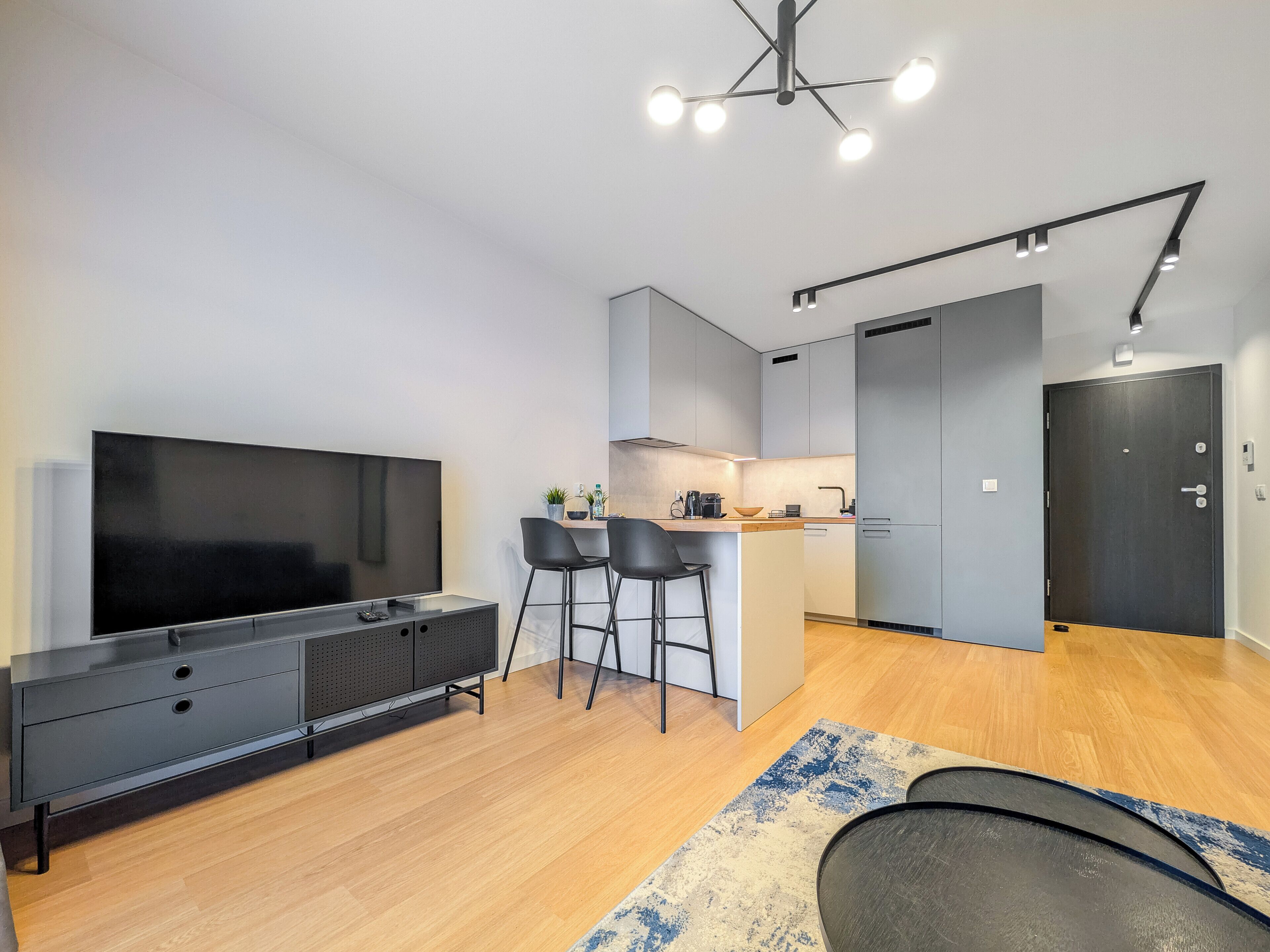 Una cocina moderna con una isla central, un comedor con taburetes de bar y un televisor de pantalla plana grande.