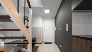 A modern interior with a wooden staircase, a dark wall with a built-in stove, and a marble floor. - MicroHome Promenady Two-Level Apartment (Wroclaw)