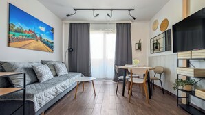 A modern living space with a sofa, dining table, chairs, and a TV. - MicroHome Promenady Two-Level Apartment (Wroclaw)