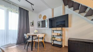 A modern living room with a dining area, wooden flooring, a flat-screen TV mounted on the wall, and a staircase leading to an upper level. - MicroHome Promenady Two-Level Apartment (Wroclaw)
