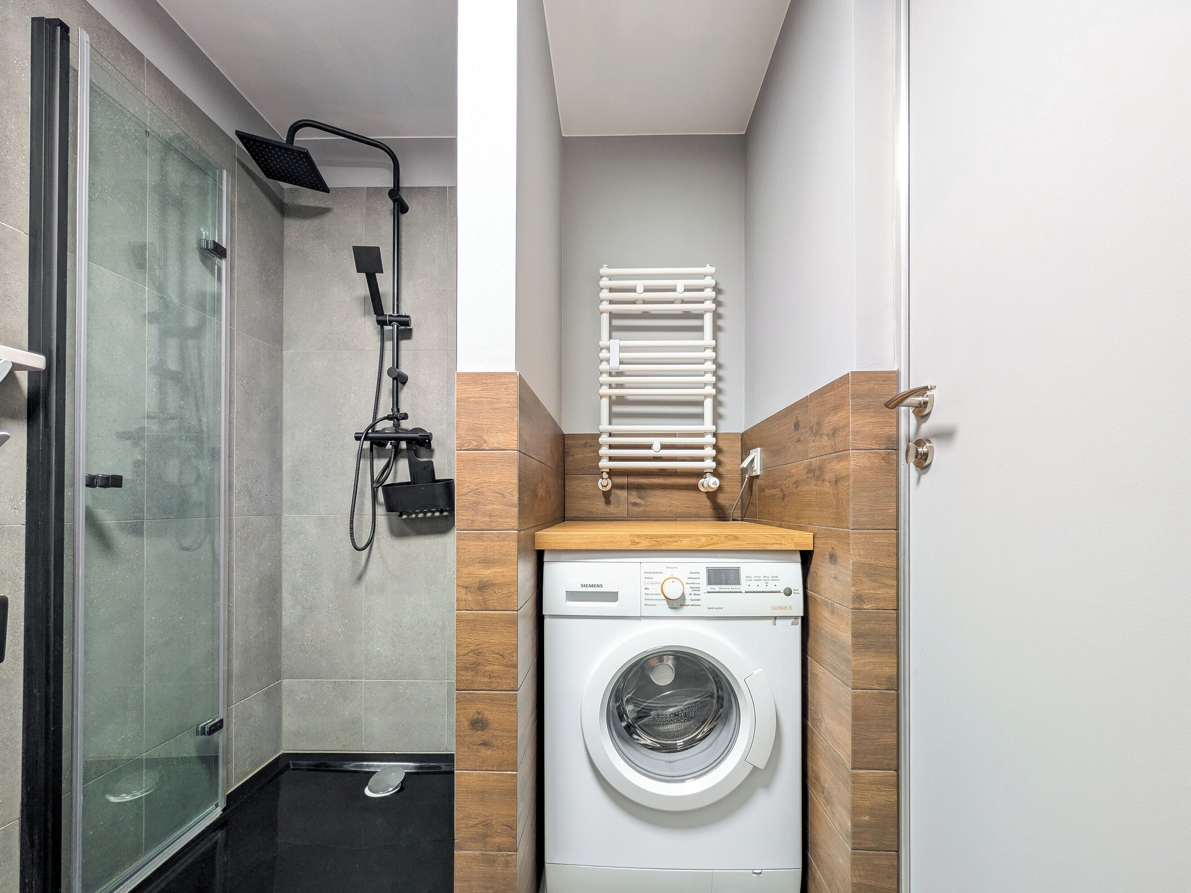 A compact bathroom with a glass-enclosed shower, a built-in washing machine, and a towel rack.