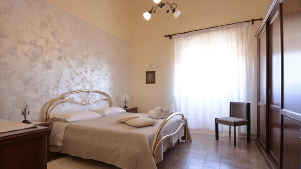 A bedroom with a bed, a chair, a nightstand, a lamp, a window with curtains, and a wall with a textured pattern. - Amazing apartment in Suni with WiFi (Suni)