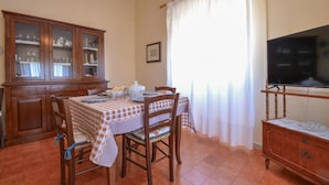 A dining area with a table set for two, a wooden cabinet with glass doors, a television on a stand, and a window with curtains. - Amazing apartment in Suni with WiFi (Suni)