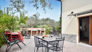 An outdoor patio with a brick barbecue, metal chairs, and a table set for dining. - Pet friendly apartment (Santo Stefano Di Magra)