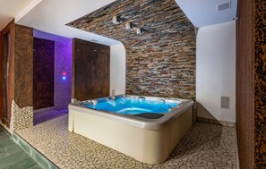 A spa area with a hot tub, stone walls, and a tiled floor.