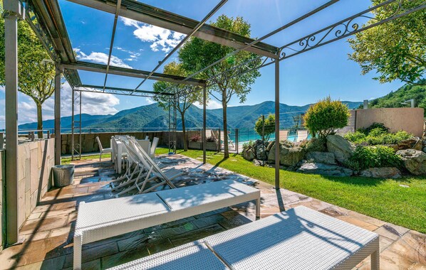 A covered outdoor area with a pool, lounge chairs, and a view of mountains.