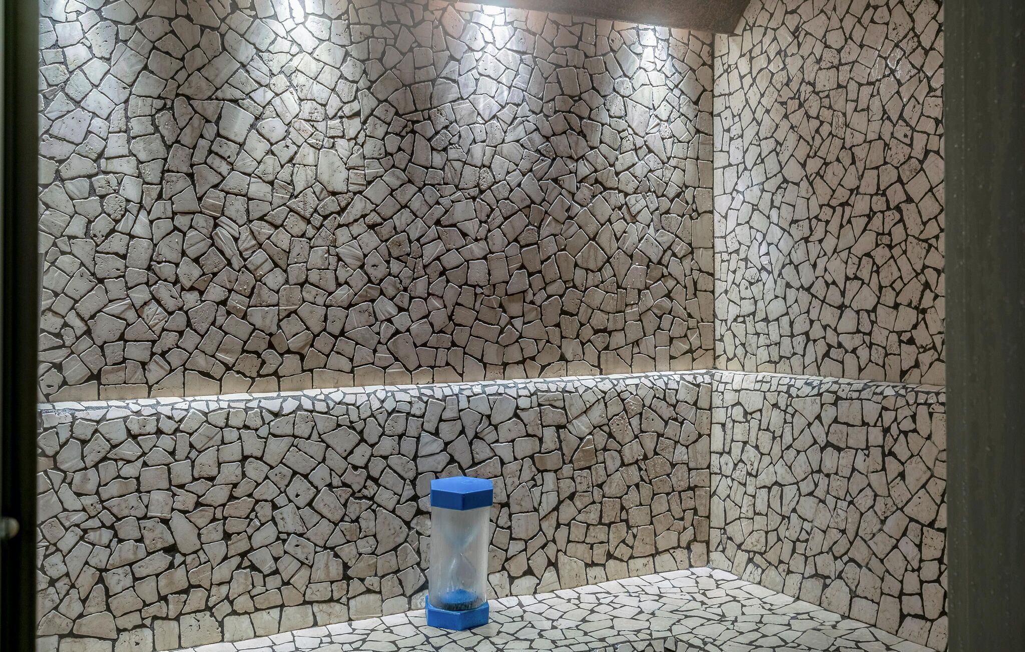 Une salle de bain avec des murs recouverts de mosaïques et une poubelle bleue.