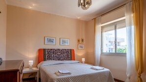 Un dormitorio con cama, lámparas de noche, una ventana con cortinas e imágenes enmarcadas en la pared.