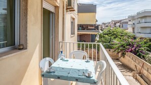 Un balcón con una mesa preparada para dos, sillas blancas y vistas a edificios y zonas verdes cercanas.