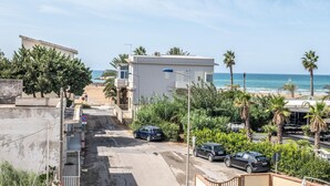 Una calle costera con edificios, coches aparcados y una playa al fondo.