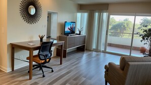 Ein modernes Wohnzimmer mit einem Holztisch, einem bequemen Sessel, einem Flachbildfernseher, einem großen Spiegel und einer Glastür zum Balkon.