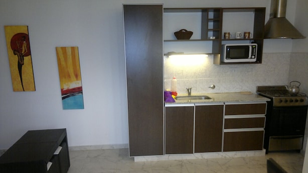 A compact kitchen with a microwave, stove, and sink. There are two paintings on the wall and a bench in the corner. - Apart A Orillas del Mar (Costa Azul)