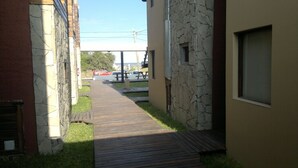 A narrow pathway leading to a picnic area with a stone wall on one side and a building on the other. - Apart A Orillas del Mar (Costa Azul)