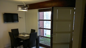 A dining area with a table and chairs, a television mounted on the wall, and a window with blinds. - Apart A Orillas del Mar (Costa Azul)