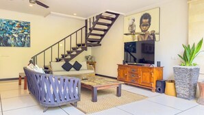 Una sala de estar moderna con una escalera, un sofá, una mesa de centro, un televisor y un cuadro grande.