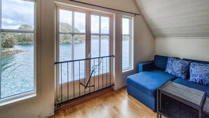 A room with a wooden floor, a blue sofa, and large windows overlooking a body of water. - 2 bedroom stunning home in Lepsøy (Lepsøy)