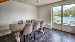 A dining area with a wooden table and six chairs, a potted plant, and a view of a lake through a glass door. - 2 bedroom stunning home in Lepsøy (Lepsøy)