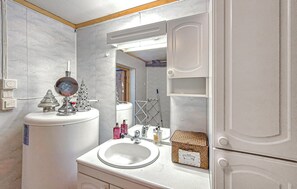 Un baño con lavamanos, espejo y armarios blancos. Hay un pequeño árbol de Navidad sobre la encimera y una cesta con artículos de aseo.