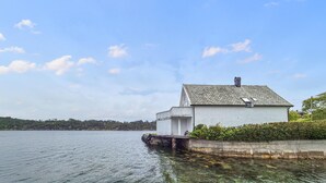 Un bâtiment blanc, doté d’un toit en tuiles, se dresse au bord d’un lac paisible, entouré de verdure.