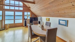 Un espace repas comprenant une table, des chaises et une vue sur la mer grâce à de grandes fenêtres.