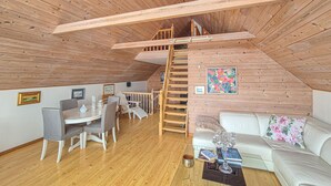 Une pièce de style « loft », avec un plafond en bois, un coin repas comprenant une table et des chaises, un escalier et un canapé.
