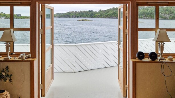 Une cabane en bois dotée d’une terrasse donnant sur un lac, avec deux lampes et un haut-parleur placés sur le rebord de la fenêtre.