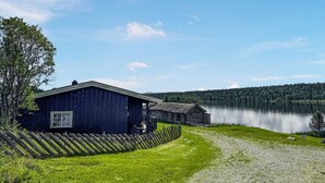 Ein rustikales Holzhäuschen mit Kiesweg und einem friedlichen See im Hintergrund.