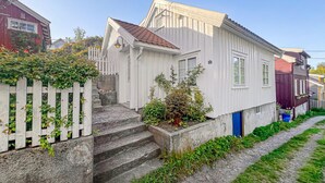 Een wit huis met één verdieping, met een rood dak, een witte schutting en een betonnen trap naar de voordeur.