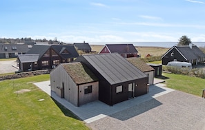A modern building with a sloped roof, a gravel driveway, and a view of the sea.