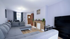 A modern living room with a grey sectional sofa, a fireplace, a flat-screen TV, and a door leading to another room. - 3-bed House - Sleeps 7, Parking & Views (Belvedere)