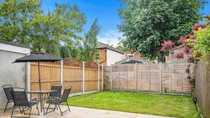 A backyard patio with a table and chairs, a wooden fence, and a grassy lawn. - 3-bed House - Sleeps 7, Parking & Views (Belvedere)