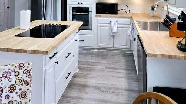 A modern kitchen with white cabinets, a built-in oven, a microwave, and a wooden countertop.
