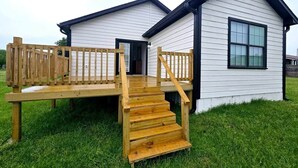 A two-story wooden house with a wooden deck and stairs leading to the entrance.