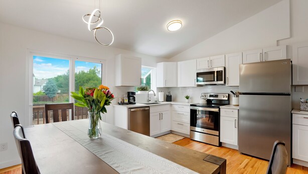 A modern kitchen with white cabinets, stainless steel appliances, and a dining area with a table and chairs. - Stylish 4BR Retreat - Hot Tub, Game Room & Modern Comforts (Westminster)