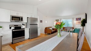 A modern kitchen with white cabinets, stainless steel appliances, and a wooden dining table with a vase of flowers. - Stylish 4BR Retreat - Hot Tub, Game Room & Modern Comforts (Westminster)