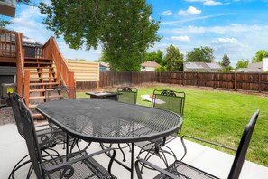 Een achtertuin met een terras, een ronde metalen tafel en stoelen, een houten terras en een houten omheining.