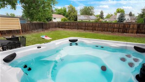 A hot tub with jets, surrounded by a wooden fence, a grassy yard, and houses in the background. - Stylish 4BR Retreat - Hot Tub, Game Room & Modern Comforts (Westminster)
