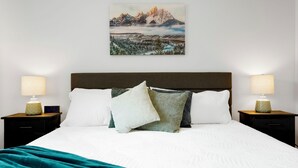 A hotel room with a large bed, two bedside tables with lamps, a painting of a mountain landscape on the wall, and a teal throw blanket on the bed. - Stylish 4BR Retreat - Hot Tub, Game Room & Modern Comforts (Westminster)