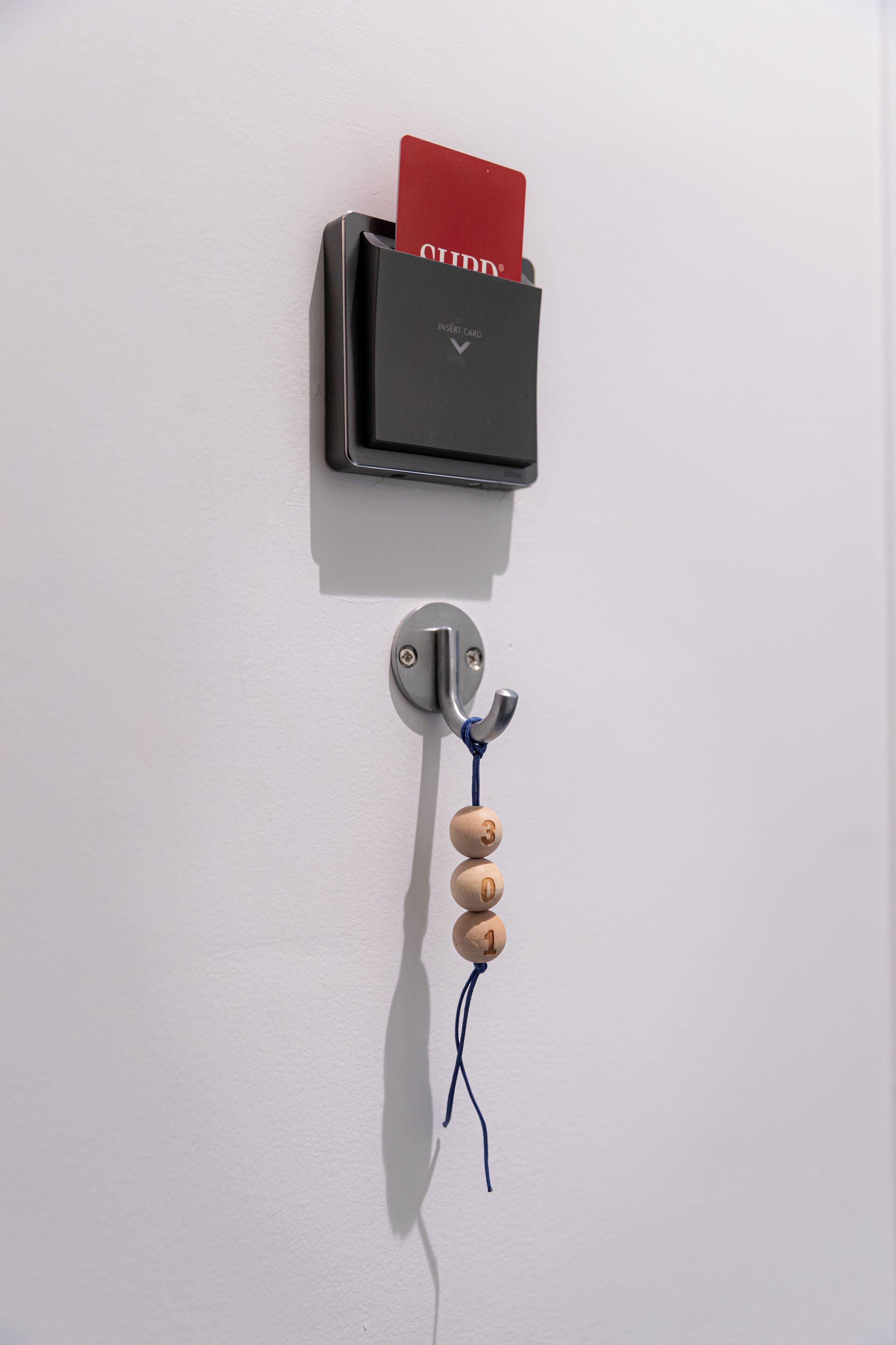 Een kaartlezer bevestigd aan een muur, met een rode kaart erin, een metalen haak en houten kralen.