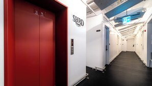 A hotel corridor with a red elevator, a SHRD Hotel sign, and an emergency exit sign. - Small House Big Door Myeongdong (Seoul)