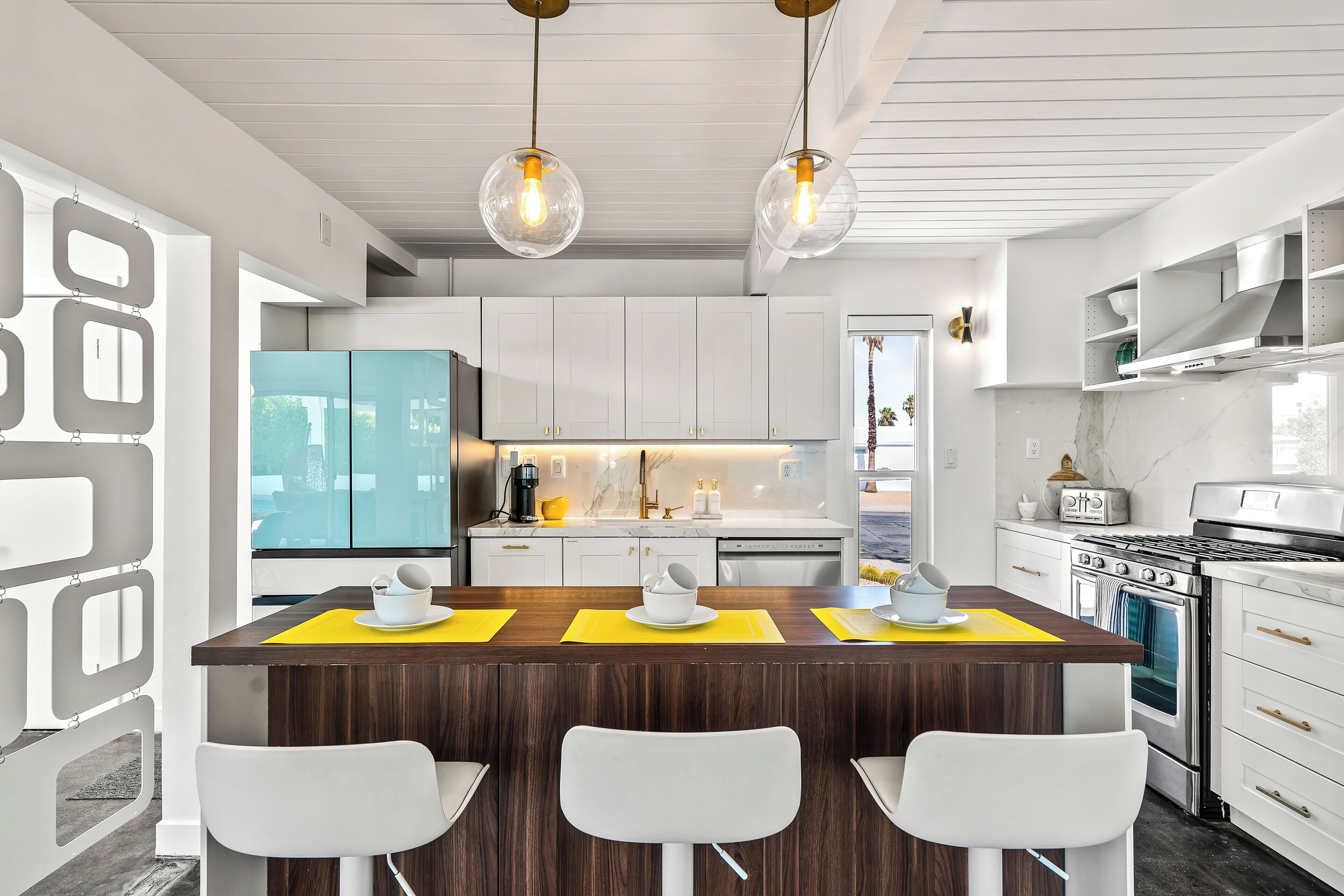 Une cuisine moderne avec des meubles blancs, un îlot central doté de tabourets et des luminaires suspendus.