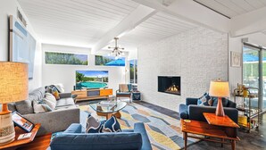 Una sala moderna con chimenea, asientos cómodos y un gran ventanal con vista a una piscina.
