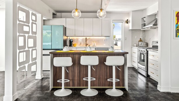Una cocina moderna con armarios blancos, una isla central con taburetes altos e iluminación colgante.