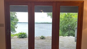 Una porta in legno con pannelli di vetro che dà su un patio con vista su un lago e alberi.