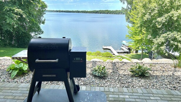 Un barbecue Traeger su un patio con vista su un lago, un pontile e sedie da pontile.