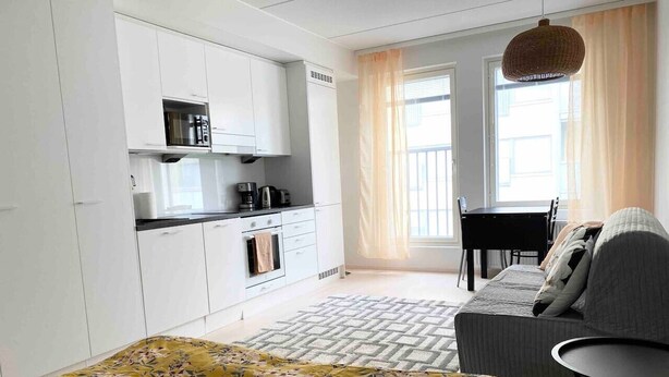 Une pièce de taille modeste comprenant un lit, une petite kitchenette, un coin repas et une fenêtre avec des rideaux.