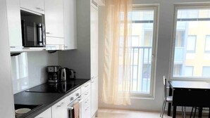 Une cuisine moderne avec des armoires blanches, un comptoir noir et une machine à café. Un tapis à motifs recouvre le sol et une fenêtre est agrémentée de rideaux.