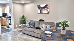 Ein modernes Wohnzimmer mit einem grauen Sofa, Zierkissen, einem Couchtisch und einem an der Wand hängenden abstrakten Gemälde.