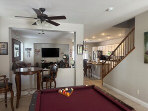 A living room with a pool table, a ceiling fan, and a television.