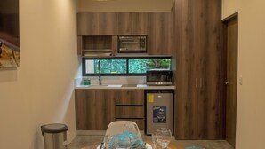 A dining area with a wooden table set for two, a kitchen in the background, and a hanging light fixture.